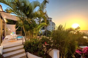 Une terrasse extérieure moderne avec une piscine, des palmiers et une vue sur le coucher de soleil.