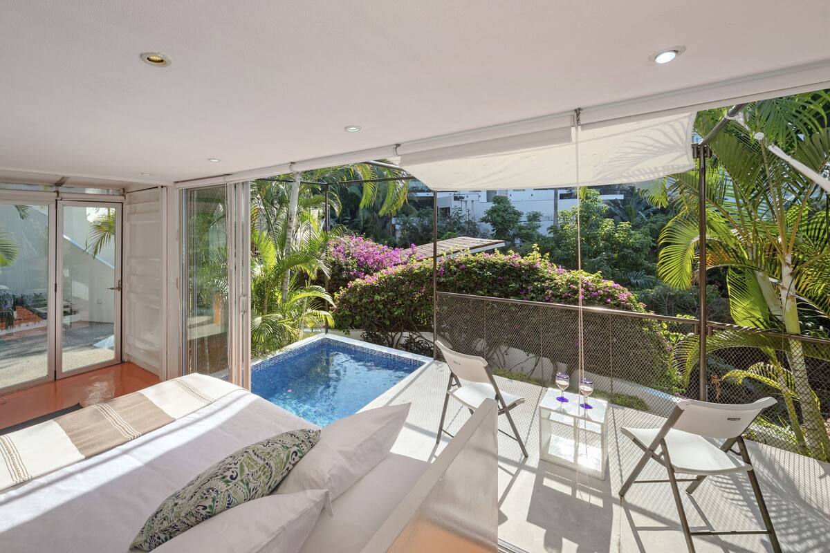 Ein moderner Poolbereich im Freien mit Glasveranda, weißen Liegestühlen und einem Tisch mit Getränken.