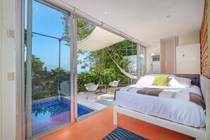 Une chambre moderne dotée d’une porte en verre donnant sur un espace piscine, d’un lit avec une literie blanche et offrant une vue sur la verdure environnante.