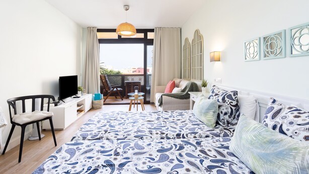 Un dormitorio con una cama grande, televisión, escritorio y balcón con vistas.