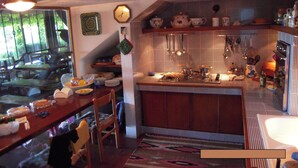 A kitchen with a stove, sink, and various kitchen utensils. There is a dining table with chairs and a window with curtains. - Il Riccio holiday home (Monte Argentario)