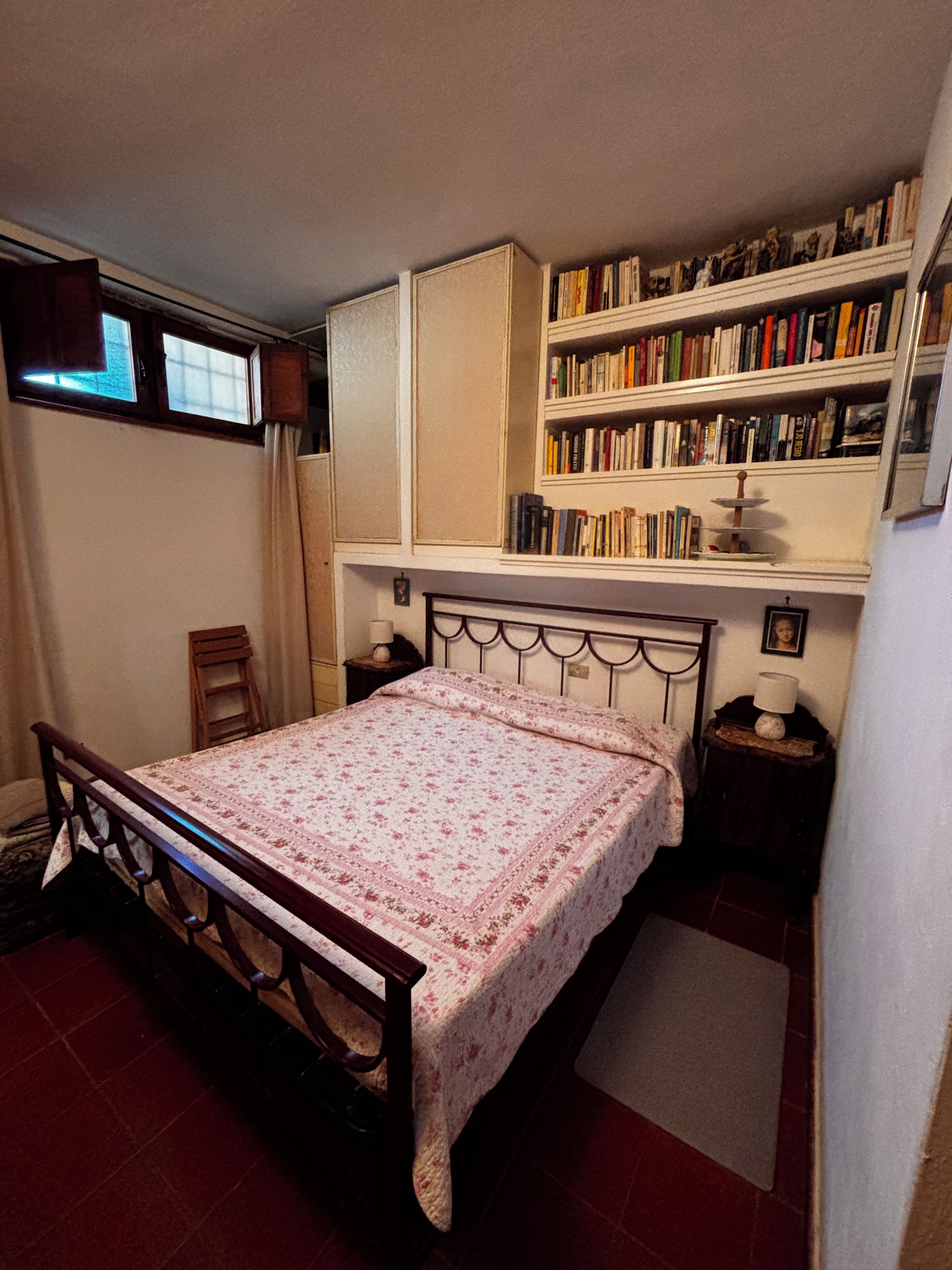 Ein Schlafzimmer mit einem Bett, einem Bücherregal, einem Fenster und einer Tür.