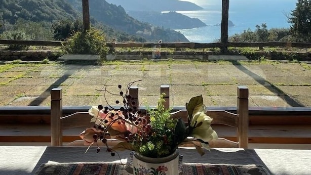 A table with a floral vase and a patterned tablecloth, overlooking a scenic coastal view with mountains and the sea. - Il Riccio holiday home (Monte Argentario)