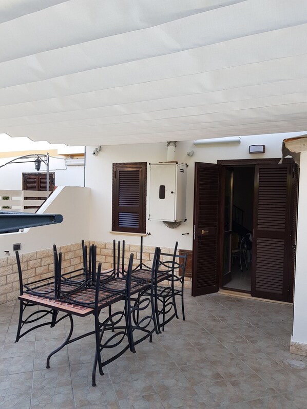 A covered outdoor patio with a table and chairs, a water pipe, and a door leading to an interior space.