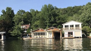 A houseboat with a balcony and a garage, surrounded by water and trees.