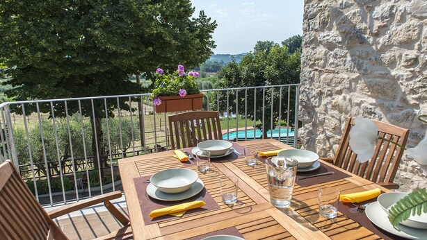 Tavolo in legno apparecchiato per la cena, con piatti, bicchieri e posate, con vista su una piscina e sul verde.