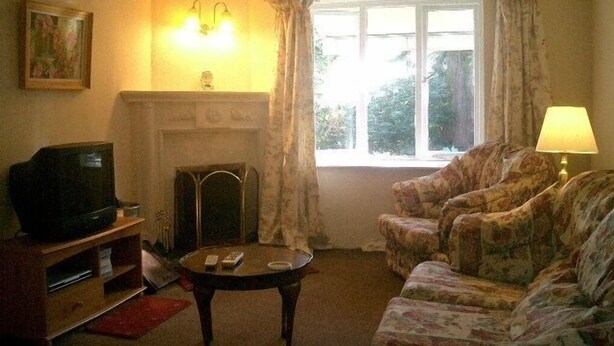 A living room with a fireplace, a television, a sofa, and a window with curtains. - Pool Cottage  (Machynlleth)