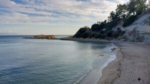 Una spiaggia con acque cristalline, una riva sabbiosa e un promontorio roccioso all'orizzonte.