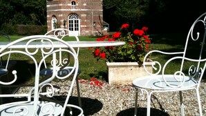 A garden with a stone building, two white metal chairs, and red flowers. - XVII century dovecote (Grémonville)