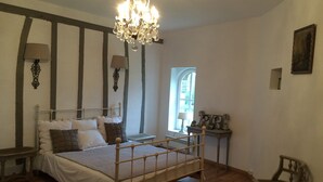 A bedroom with a wooden bed, a chandelier, a window, and a small table with a lamp. - XVII century dovecote (Grémonville)