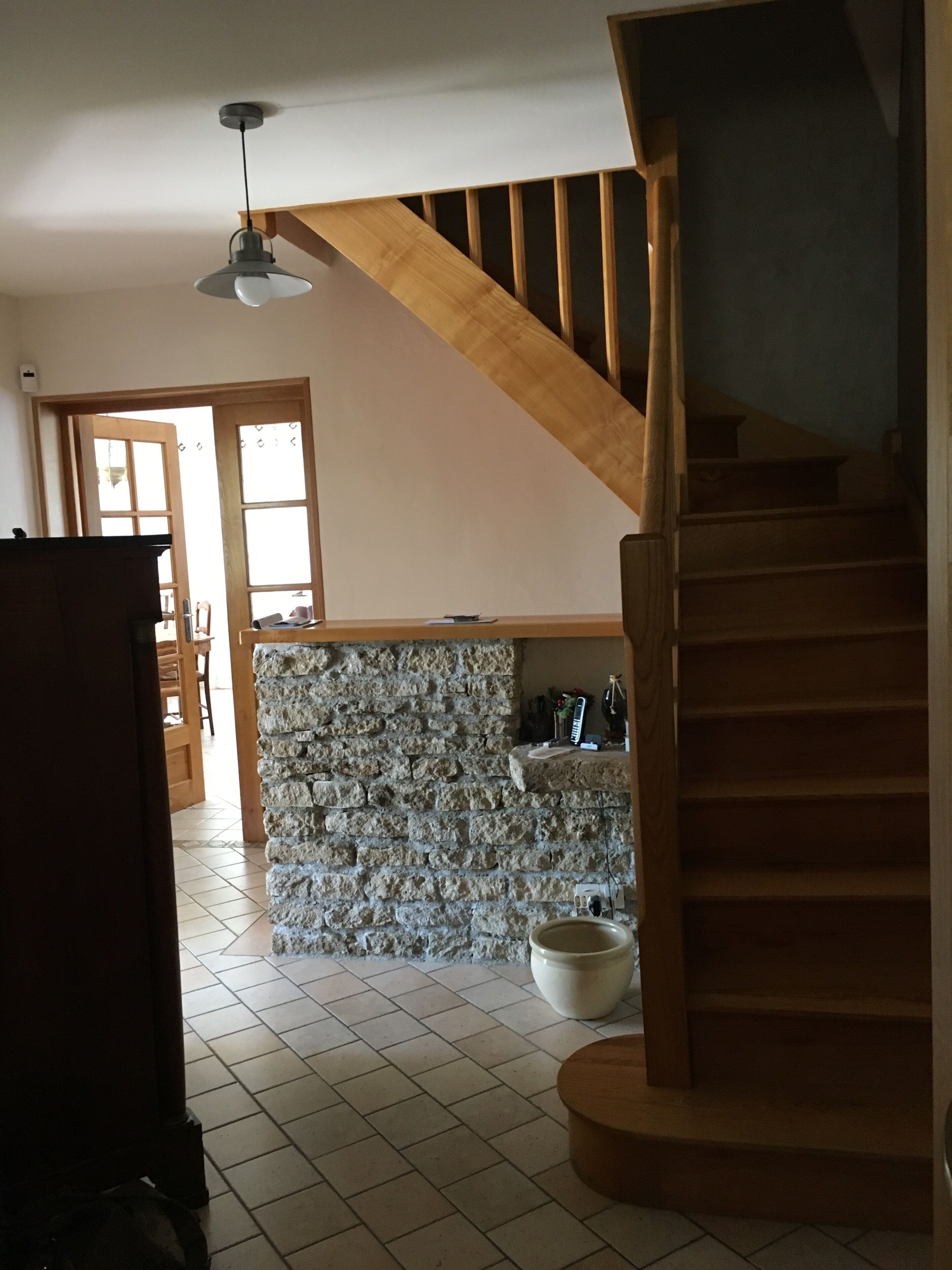 Eine Treppe führt zu einer zweiten Etage, eine Steinsäule und ein Fliesenboden sind zu sehen.