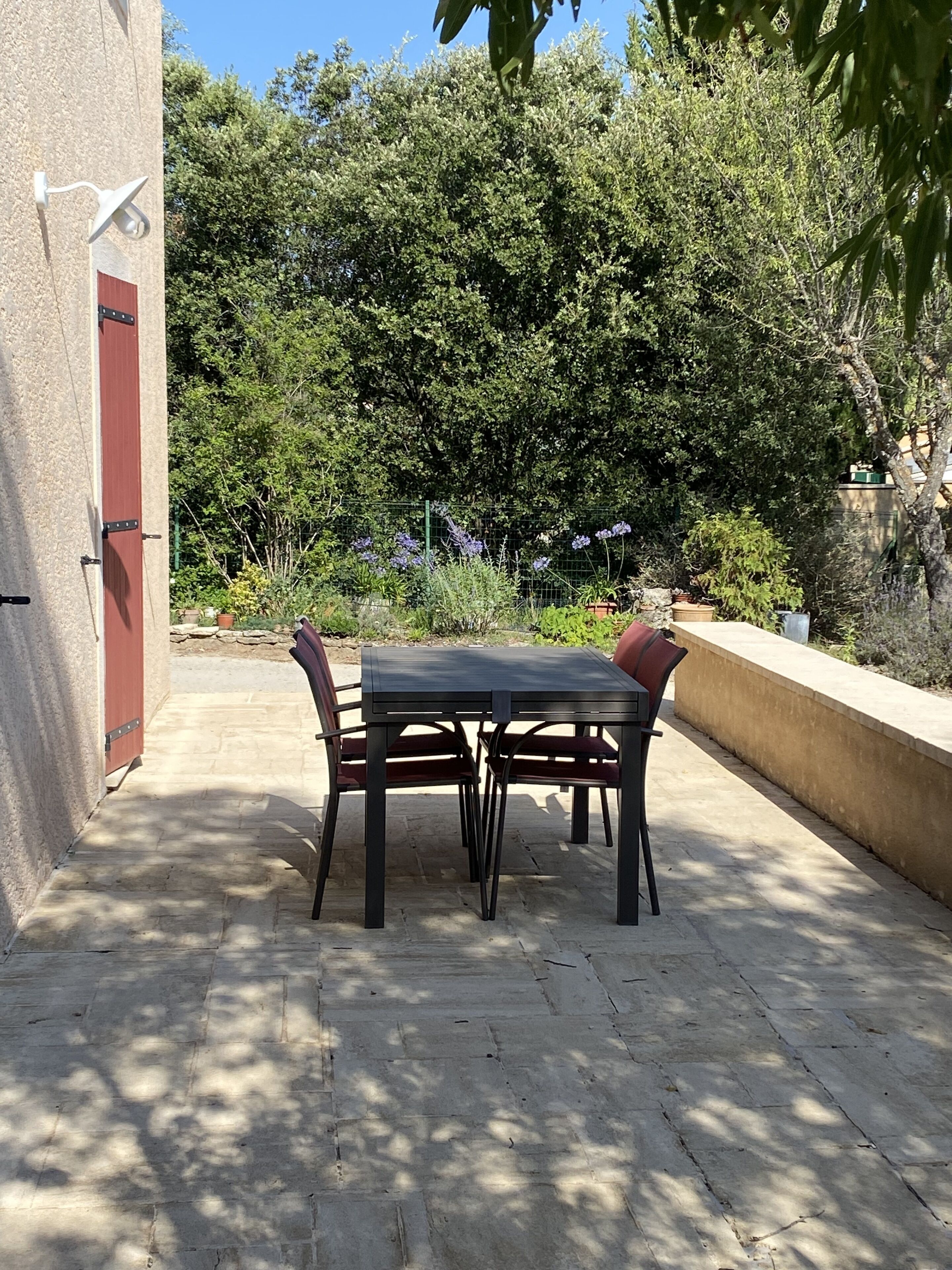 Una terrazza esterna con tavolo e sedie, circondata da un giardino con diverse piante e un recinto.