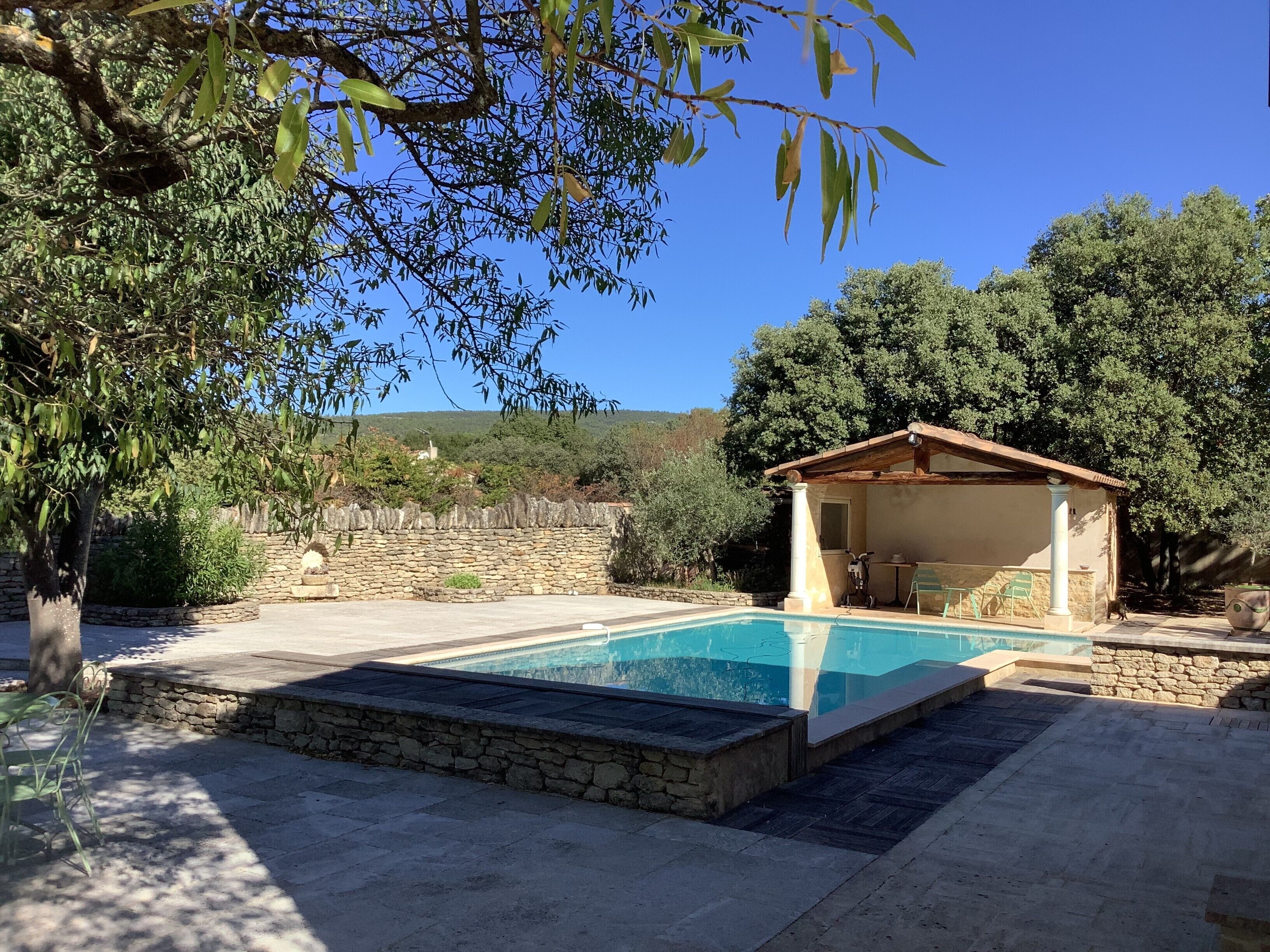 A pool area with stone walls, a covered seating area, and surrounding greenery.