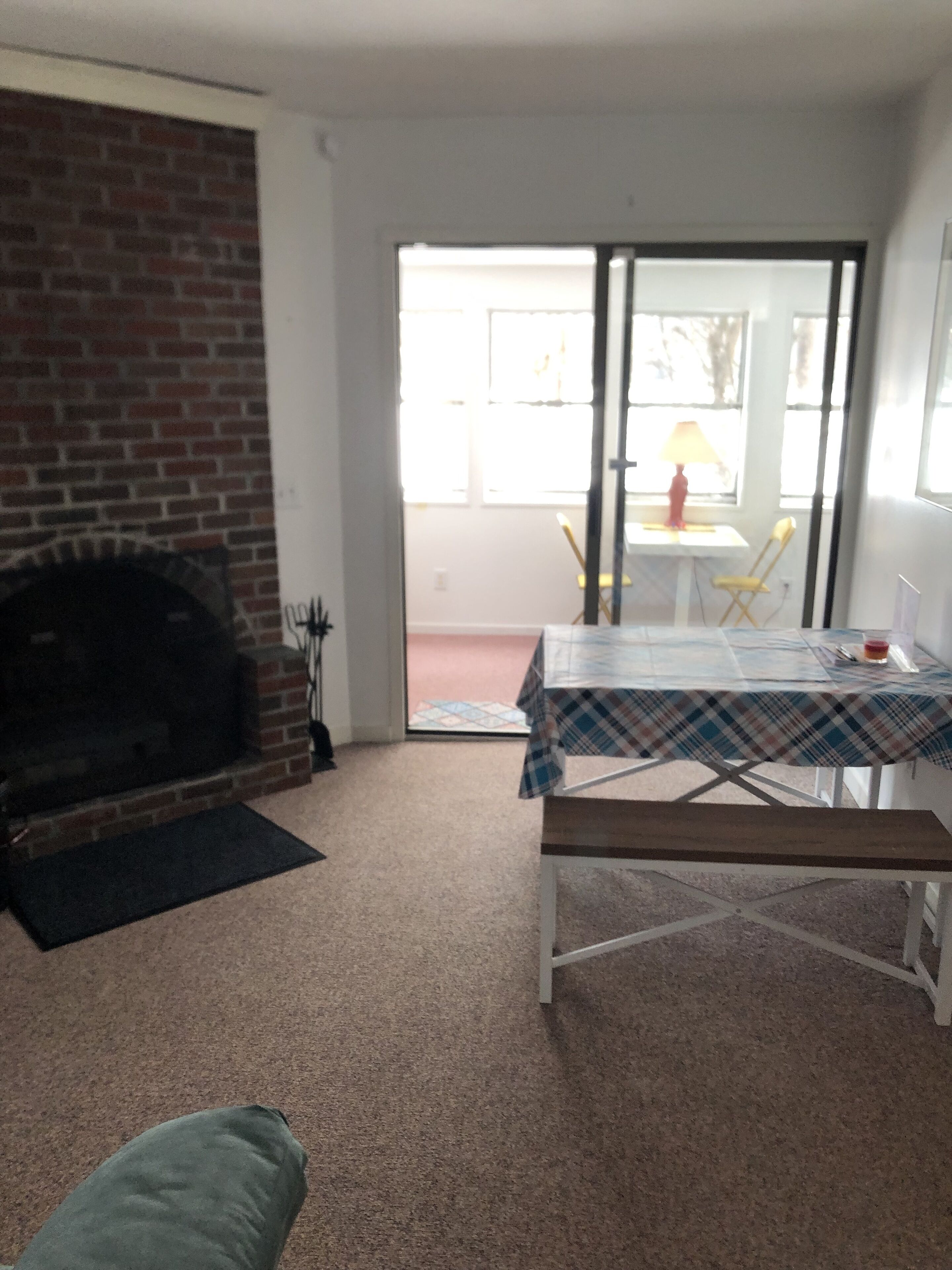 Un salon doté d’une cheminée, une table à manger recouverte d’une nappe à carreaux et une porte-fenêtre coulissante donnant sur un espace extérieur avec une chaise et une table.