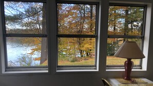 Una stanza con tre finestre vista su un lago e il foliage autunnale. Una lampada è posata su un tavolo vicino alle finestre.