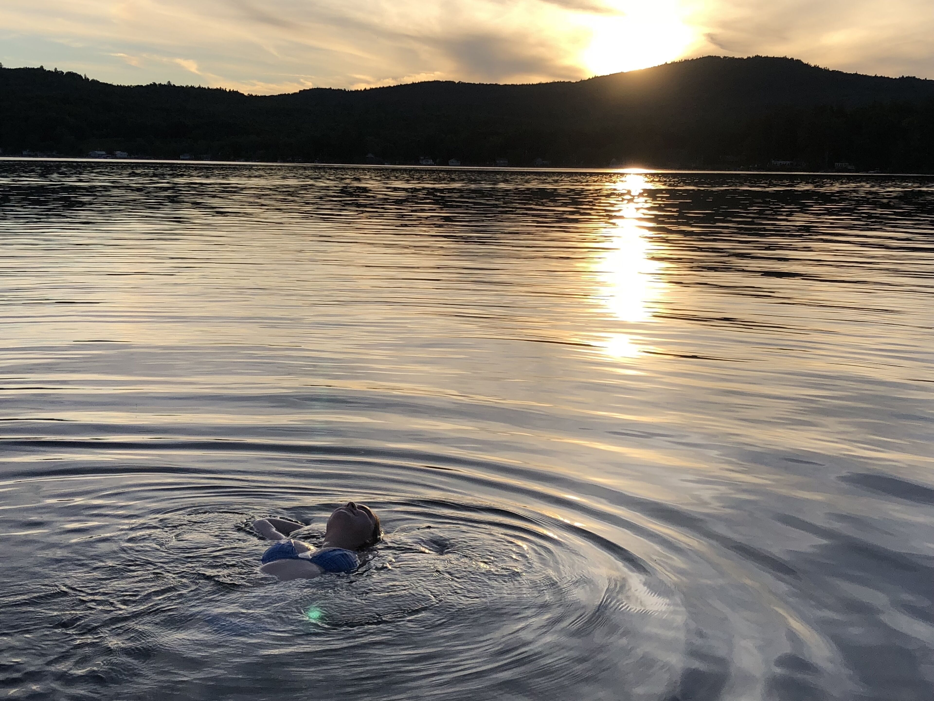 A calm lake with a person swimming in the foreground.