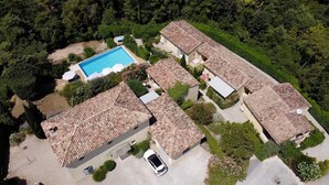 Vista aérea de una zona residencial con piscina, casas de techo de teja terracota y abundante vegetación.