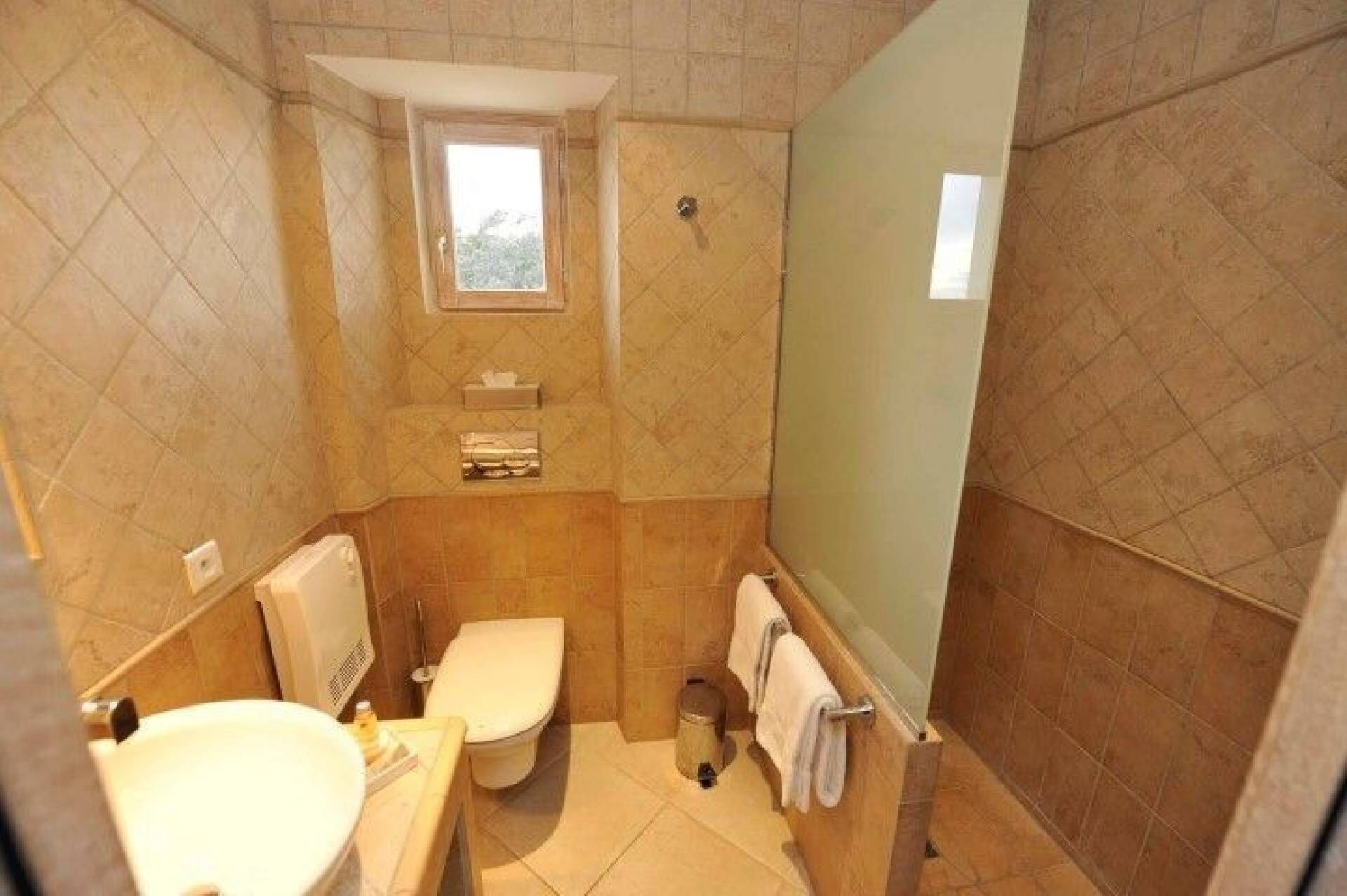 A small, tiled bathroom with a toilet, sink, and a window.
