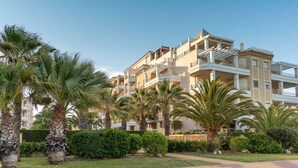 Ein mehrstöckiges Hotel mit Balkonen, Palmen und einem gepflegten Garten.