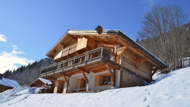 Un chalet en bois doté d’un balcon, niché au cœur d’un paysage enneigé.