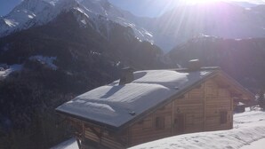 Une cabane en bois, dont le toit est recouvert de neige, entourée de montagnes et sous un ciel dégagé.