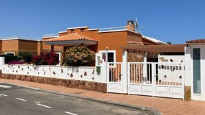 A modern house with a stone wall, a gated entrance, and a clear blue sky. - Casa Piedra - Air Conditioned, Private Pool, Spa,  Pool Table, Frontline Golf (Caleta De Fuste)
