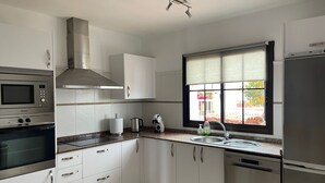 A modern kitchen with white cabinets, stainless steel appliances, a window with blinds, and a countertop with a kettle and dish soap. - Casa Piedra - Air Conditioned, Private Pool, Spa,  Pool Table, Frontline Golf (Caleta De Fuste)