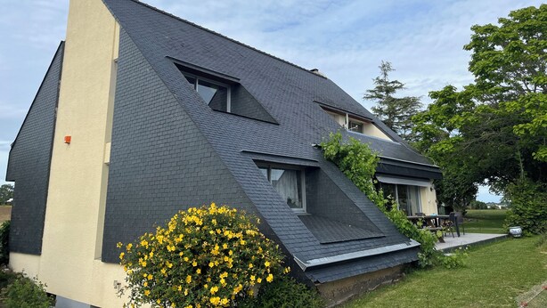 Une maison moderne avec un toit à forte pente, une cheminée bien visible et une petite fenêtre.