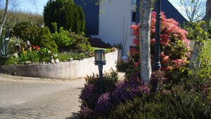 Un chemin pavé mène à un bâtiment doté d’un jardin où l’on peut admirer différentes plantes et fleurs.
