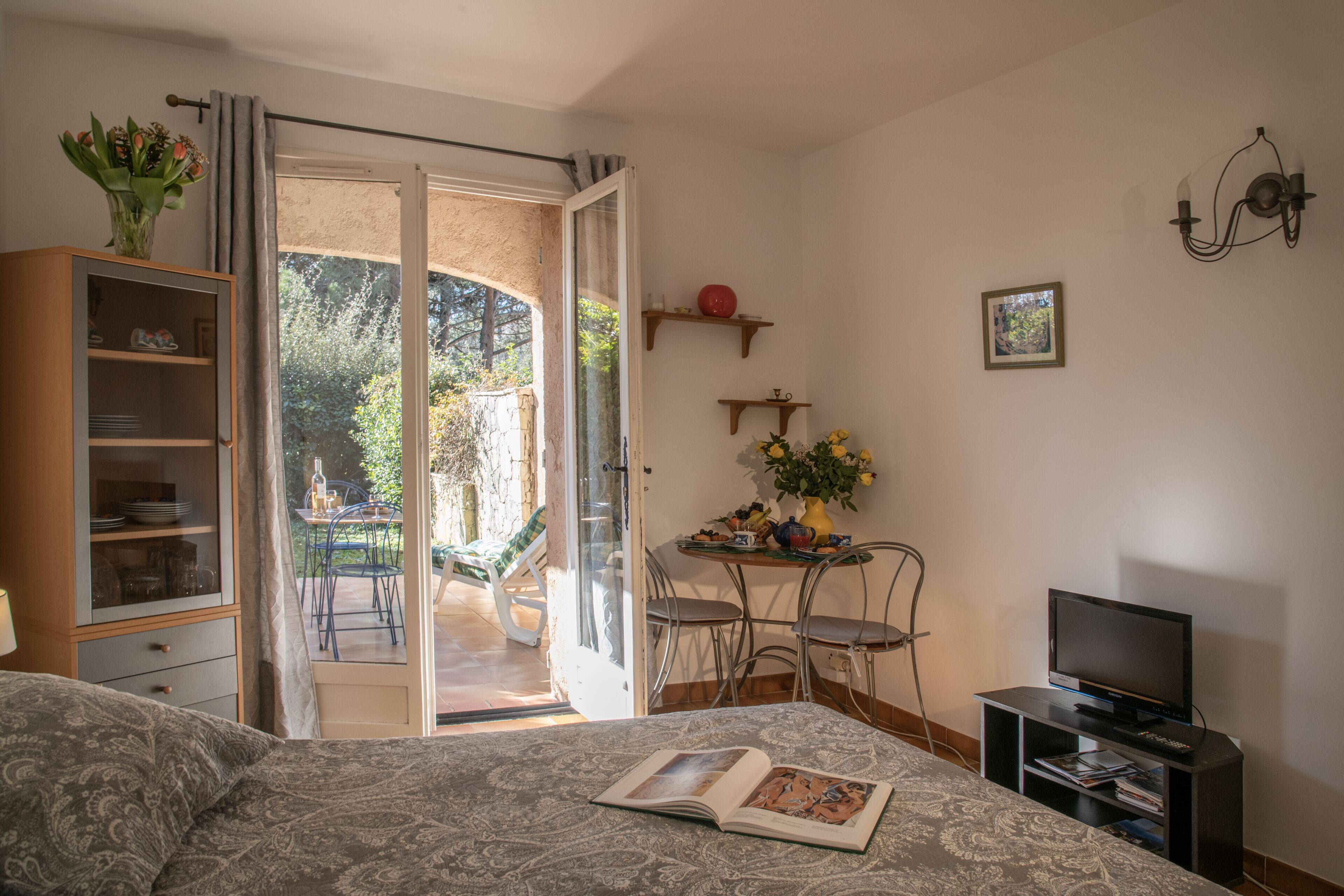 Un dormitorio con cama, un mueble para televisor, una estantería y un comedor con mesa y sillas.
