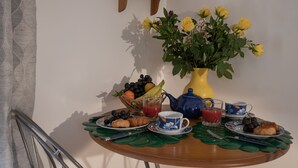 Ett frukostbord med croissanter, en fruktskål, en vas med blommor och en tekanna.