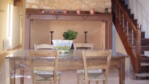 Un comedor con pared de piedra, sillas de madera, mesa de vidrio y una escalera de madera.