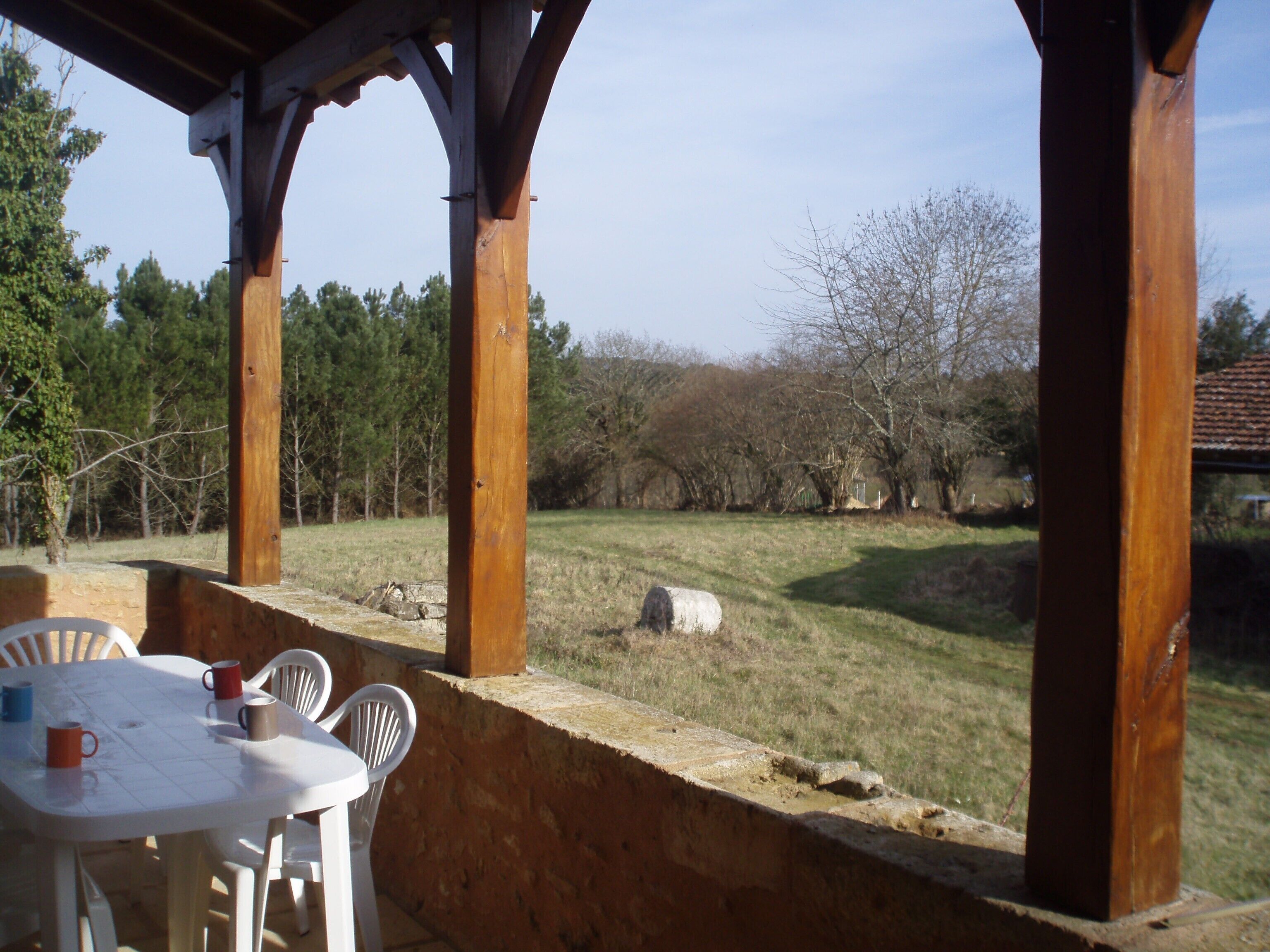 Eine Terrassensitzgruppe mit Tisch und Stühlen mit Blick auf eine Rasenfläche mit Bäumen und einer Steinmauer.