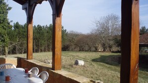 Un patio al aire libre con una mesa y sillas, con vista a una zona verde con árboles y un muro de piedra.