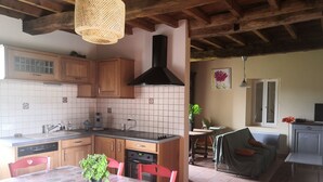 Una cocina con armarios de madera, salpicadero de azulejos, lámpara colgante y un comedor con mesa y sillas.