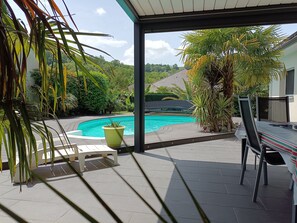 Un espacio al aire libre techado con piscina, rodeado de vegetación y vistas a una colina.