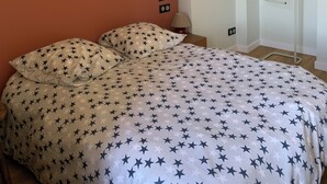 Een slaapkamer met een bed, beddengoed met sterafdruk, een houten hoofdeinde, een lamp en een witte kledingkast.