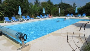 En swimmingpool med blå liggestole og parasoller, omgivet af grønt.