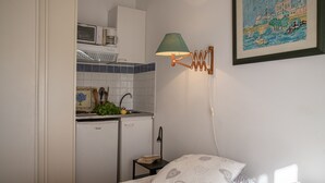 A compact room with a bed, a small kitchenette, and a wall-mounted lamp. - In villa, charming studio 2 pers with terrace in St Paul de Vence (Saint-Paul-De-Vence)