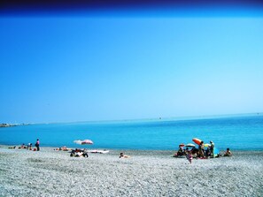 A pebbled beach with people sunbathing and swimming.
