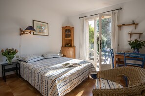 A bedroom with a bed, a wooden cabinet, a dining table with chairs, and a window with curtains.
