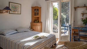 Ein Schlafzimmer mit einem Bett, einem Holzschrank, einem Korbstuhl und einem Tisch mit einer Vase.