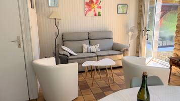 Un salon chaleureux avec un canapé gris, des fauteuils blancs, une petite table et une bouteille de vin.