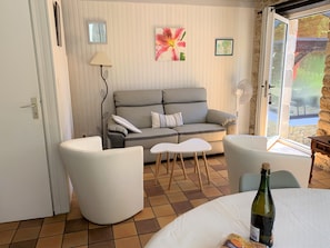 Un salon chaleureux avec un canapé gris, des fauteuils blancs, une petite table et une bouteille de vin.