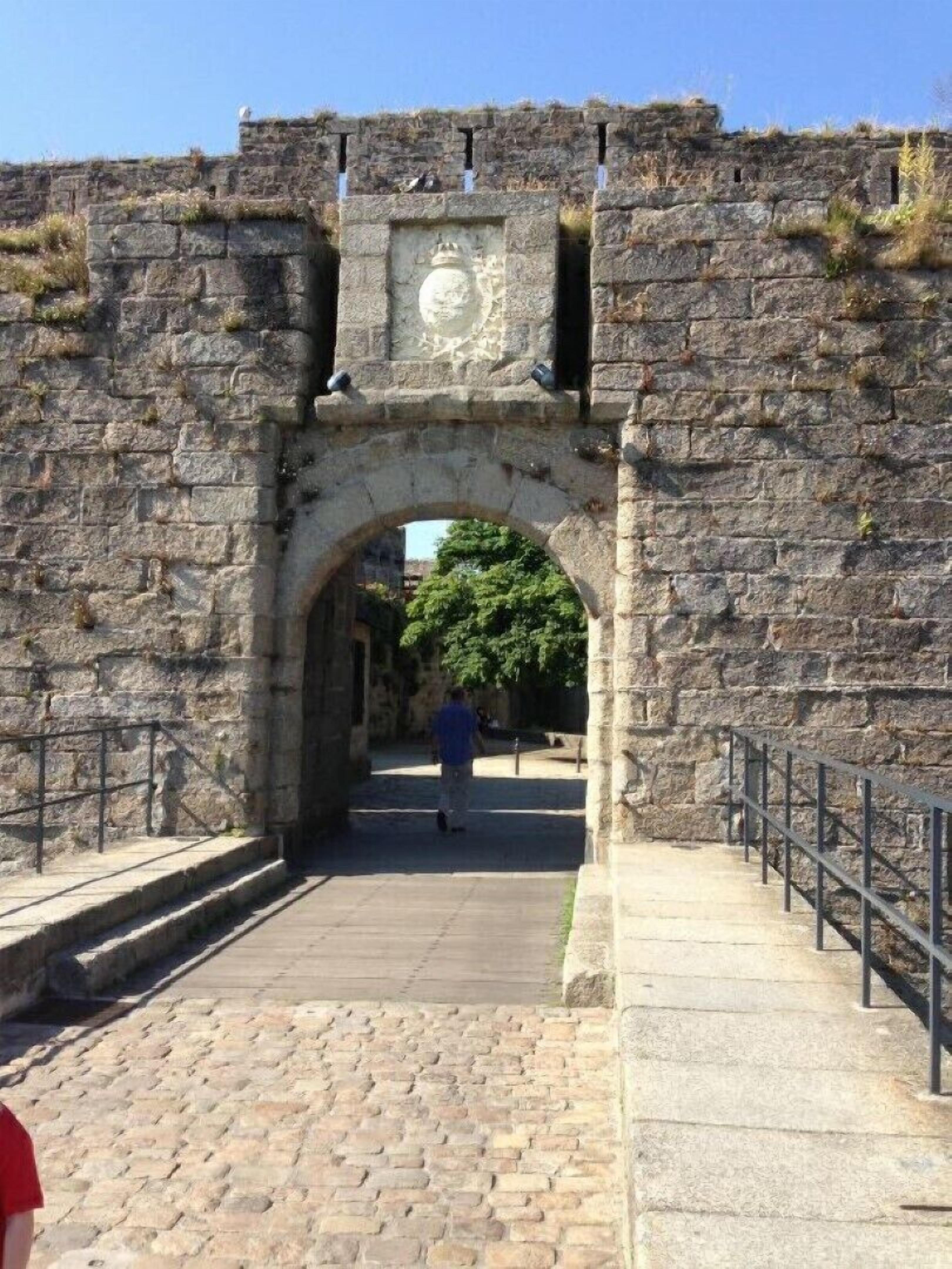 An arched stone gateway leading into a courtyard with a paved walkway and metal railings.