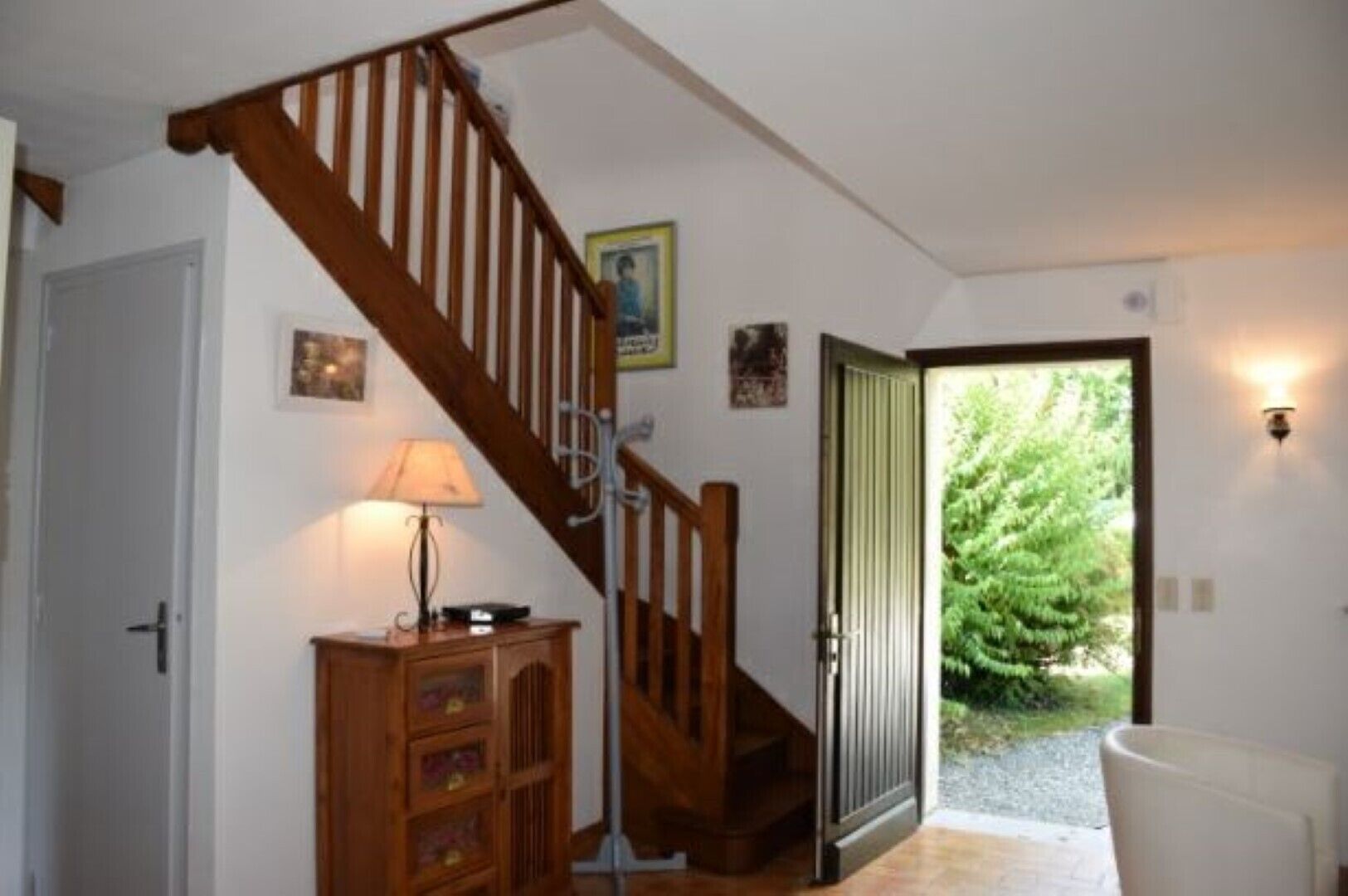A staircase with wooden railings leading to a door, a lamp on a wooden cabinet, and a view of greenery outside.