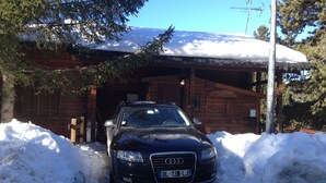 Un cotxe negre estacionat davant d'una cabana de fusta amb teulada coberta de neu.