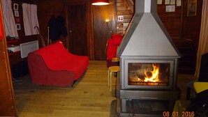 Habitació acollidora amb un foc de llenya, parets de fusta i un sofà vermell.