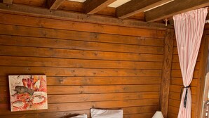 Un dormitori de cabana de fusta amb llit, una làmpada de nit, un quadre a la paret i una finestra amb cortines.