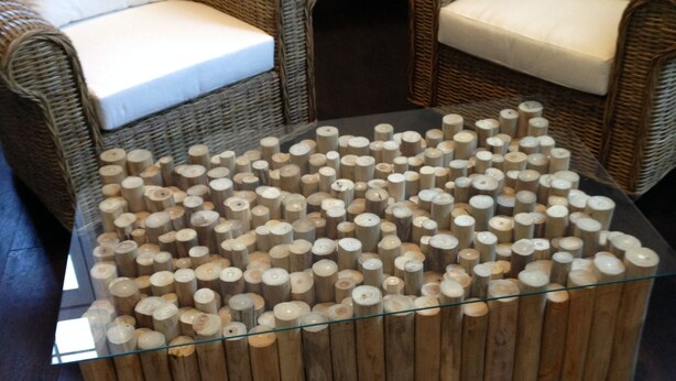 Une table basse carrée avec un plateau en verre et un socle en bois composé de troncs cylindriques.
